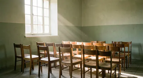 Sunlight through a plain chapel window falling on rows of simple wooden chairs.