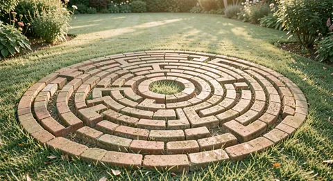 A circular brick labyrinth pattern set in a garden lawn, seen from a low standing angle at golden hour.